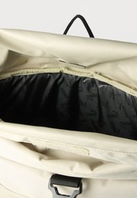 Μπεζ τσάντα με ανοιχτή κορυφή που αποκαλύπτει εσωτερική επένδυση σε μαύρο χρώμα με επαναλαμβανόμενο λογότυπο Puma, και μαύρη υφασμάτινη λαβή σε μορφή θηλιάς στο πίσω μέρος.