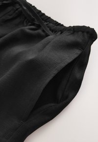 Black elastic waistband shorts made from lightweight fabric, featuring a smooth texture and folded hem. No visible patterns or hardware.