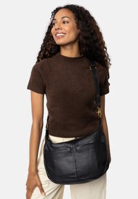 Borsa a spalla in pelle nera con una superficie liscia, caratterizzata da una forma piatta, tracolla regolabile e tasca frontale con zip.
