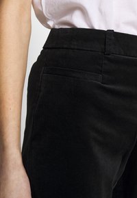 Svarta sammetbyxor med skräddarsydd passform, som har en slät yta, sidofickor och en platt midja. Ingen synlig hårdvara eller mönster.