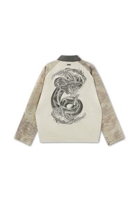 Langarmjacke mit beigen Camouflage-Ärmeln und Rückenteil, das ein detailliertes schwarz-weißes Muster mit einer gewundenen Schlange und floralen Motiven zeigt.