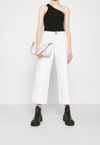 Body nera a spalla unica abbinato a pantaloni bianchi a gamba larga, con in mano una piccola borsa bianca in pelle di coccodrillo. Stivali chunky neri alla caviglia.