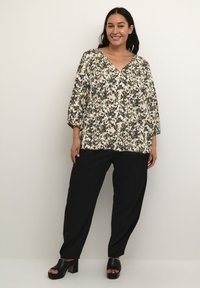 Bluse mit Blumenmuster und tiefem V-Ausschnitt, 3/4-Ärmel, kombiniert mit schwarzen Hosen und klobigen schwarzen Absatzsandalen. Glatter Stoff.