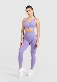 Ensemble de sport violet à côtes comprenant un top court à col en V et un legging taille haute. Le modèle porte des baskets blanches.