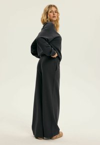 Czarny oversize sweter z wysokim kołnierzem, zestawiony z szerokimi czarnymi spodniami. Tkanina wydaje się miękka i gładka, a krój jest luźny.