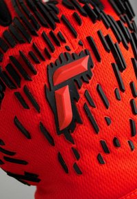 Czerwona sportowa rękawica z teksturowanymi czarnymi akcentami z gumy oraz wyraźnym czerwonym logo. Projekt zawiera wypukłe wzory zwiększające przyczepność.