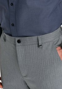 Grijze broek met een visgraatpatroon en een rechte snit, voorzien van een knoopsluiting en zijzakken, gecombineerd met een donkerblauwe gestructureerde blouse.