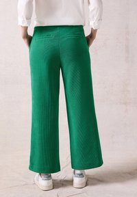 Gröna vida byxor i texturerad tyg med två bakfickor. Parat med vita sneakers med en logotyp på hälen.