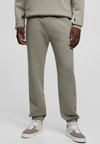 Pantalones deportivos de color verde claro hechos de mezcla de algodón, con cintura elástica, puños ajustados y bolsillos laterales. Combinados con zapatillas beige.