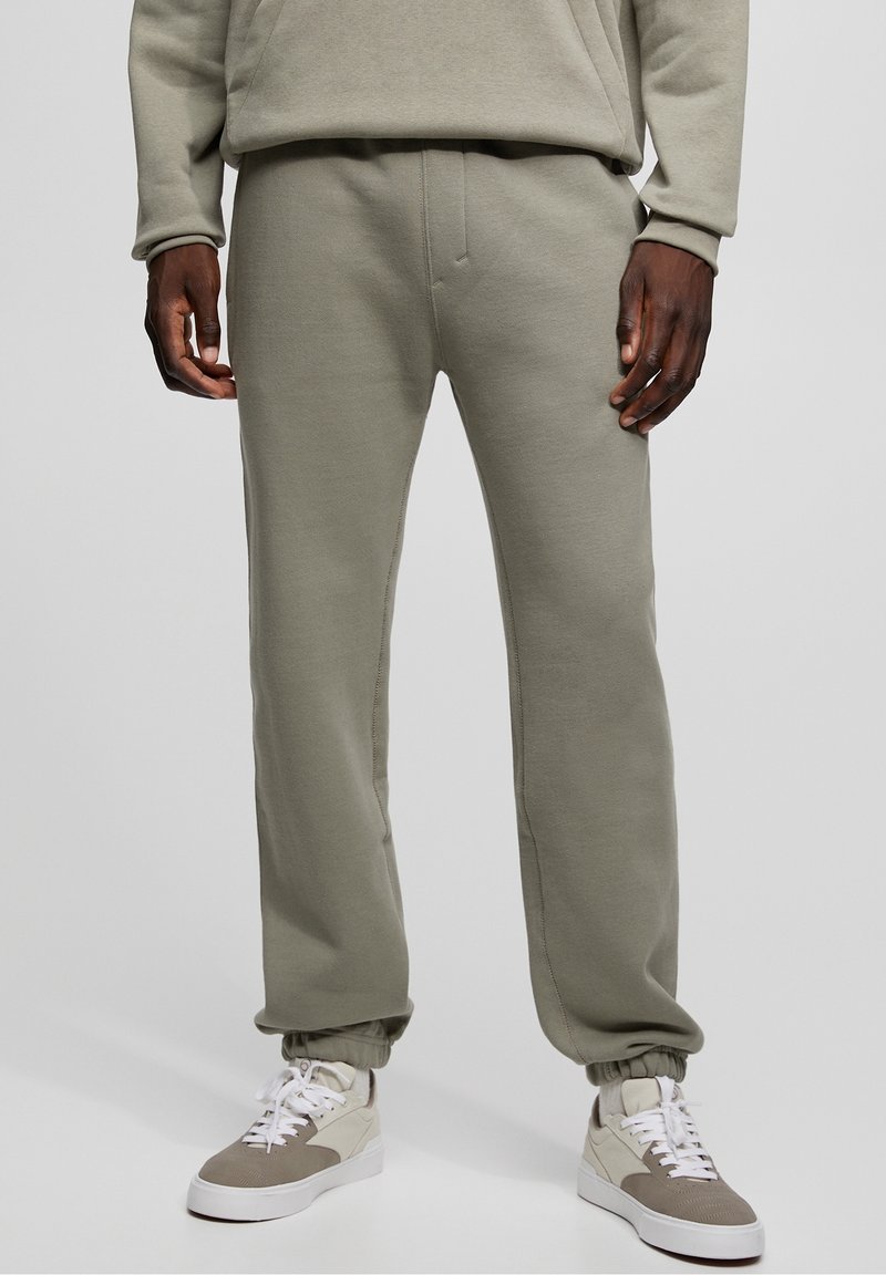 Pantalones deportivos de color verde claro hechos de mezcla de algodón, con cintura elástica, puños ajustados y bolsillos laterales. Combinados con zapatillas beige.