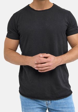 Czarny bawełniany t-shirt z okrągłym dekoltem, krótkimi rękawami i lekko zaokrąglonym dołem. Noszony z jasnoniebieskimi dżinsami.