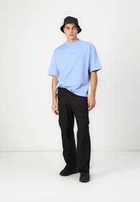 Heleheles sinine oversize t-särk, mustad cargo-püksid taskutega ja must bucket-hat. Mudel kannab musti tennisetossusid, seistes neutraalses taustas.