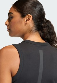 Svart ermeløs treningsgenser med rund hals og en vertikal reflekterende stripe på baksiden, laget av glatt, elastisk stoff.