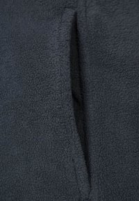 Mörkgrå fleece tyg med en vertikal ficköppning som visar mjukt, strukturerat material och sömnadsdetaljer.