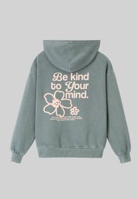 Sweat à capuche vert avec une texture douce, présentant un grand design de texte rose et des graphiques floraux au dos. Comprend un cordon de serrage sur la capuche et des poignets élastiques.