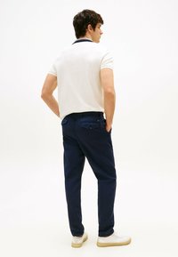 Polo bianco con colletto blu navy, pantaloni blu scuro e sneakers chiari. Look casual con una silhouette aderente e due tasche posteriori.