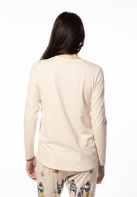 Lange mouw, lichtbeige shirt van zachte stof. Eenvoudige ronde hals, aansluitend ontwerp en een gladde textuur, met een licht gebogen zoom.