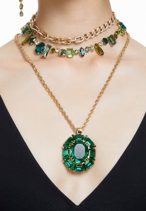 Trois colliers en or avec des pierres précieuses vertes : une chaîne épaisse, un collier ras du cou aux pierres aux formes multiples et un long pendentif avec une grande pierre taille émeraude.