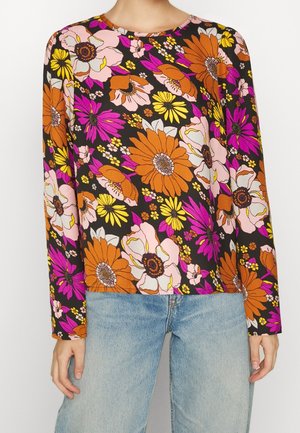 Schwarzes Langarmshirt mit großem orange-, pink-, gelb- und lila-blumigem Druck, getragen zu hellblauen Jeans.