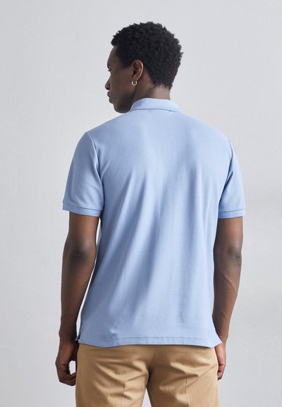 Light blue polo shirt with short sleeves, made of smooth fabric, featuring a collar and side slits, worn with beige trousers.