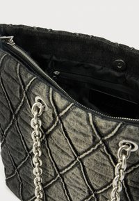 Borsa tote in denim nero trapuntato con manici a catena argentata, dotata di chiusura con zip e tasca interna, texture liscia con motivo a rombi.