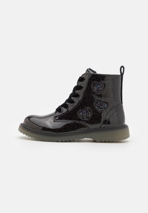 Bottines en cuir verni noir avec une finition scintillante, un design à lacets et trois découpes en forme de cœur ornées d'accents scintillants.