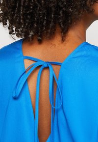 Blusa azul con una espalda profunda y abierta, con dos cordones para el cierre. Textura suave, tela ligera y diseño minimalista.