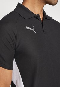 Polo noir en tissu texturé, avec un logo Puma blanc sur la poitrine et des panneaux latéraux blancs pour le contraste.