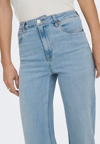 Light blue high-waisted jeans made of denim with a smooth texture, featuring a silver button, front pockets, and a clean design.