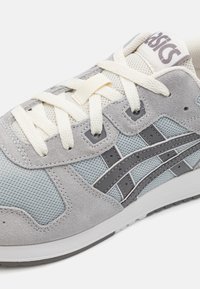 Baskets de sport grises avec une tige en suede et mesh, trois rayures gris foncé, et des lacets crème avec une semelle blanche et un logo sur la languette.