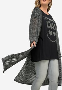Černý top s textem "Šťastný den", spárovaný s dlouhým šedým pleteným cardiganem s volnými rukávy a otevřeným předním dílem.