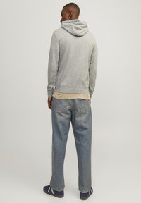 Gray hooded sweatshirt with a relaxed fit, soft fabric, and ribbed cuffs, paired with light blue loose-fitting jeans and dark shoes.