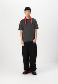 Black loose-fit pants, gray oversized t-shirt, and red bandana around the neck. Fitted black and red shoes with textured soles.