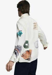 Valge pikakäise särgi seljal on mitut tekstuuri rätikud rohelises, sinises ja oranžis värvitoonis, mis kujutavad erinevaid abstraktseid mustreid.