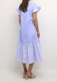 Light blue striped dress with short ruffled sleeves, flowing below-the-knee silhouette, and a textured tiered hem. Worn with beige heeled sandals.