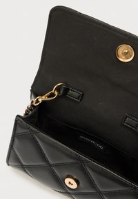 Μαύρο καπιτονέ δερμάτινο πορτοφόλι με χρυσά μεταλλικά στοιχεία, διαθέτει κούμπωμα με σούστα και αλυσίδα ιμάντα. Εσωτερικό επενδεδυμένο με μαύρο ύφασμα, με ετικέτα επωνυμίας.