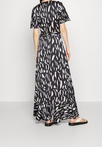 Robe maxi noire avec un motif de coups de pinceau blancs. Manches courtes, taille cintrée et ourlet évasé. Associée à des sandales plates neutres.