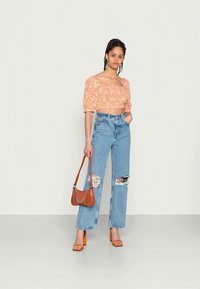 Top cropped floral laranja com mangas bufantes, combinado com jeans azuis claros rasgados de perna reta. Uma bolsa castanha e saltos block laranja completam o visual.