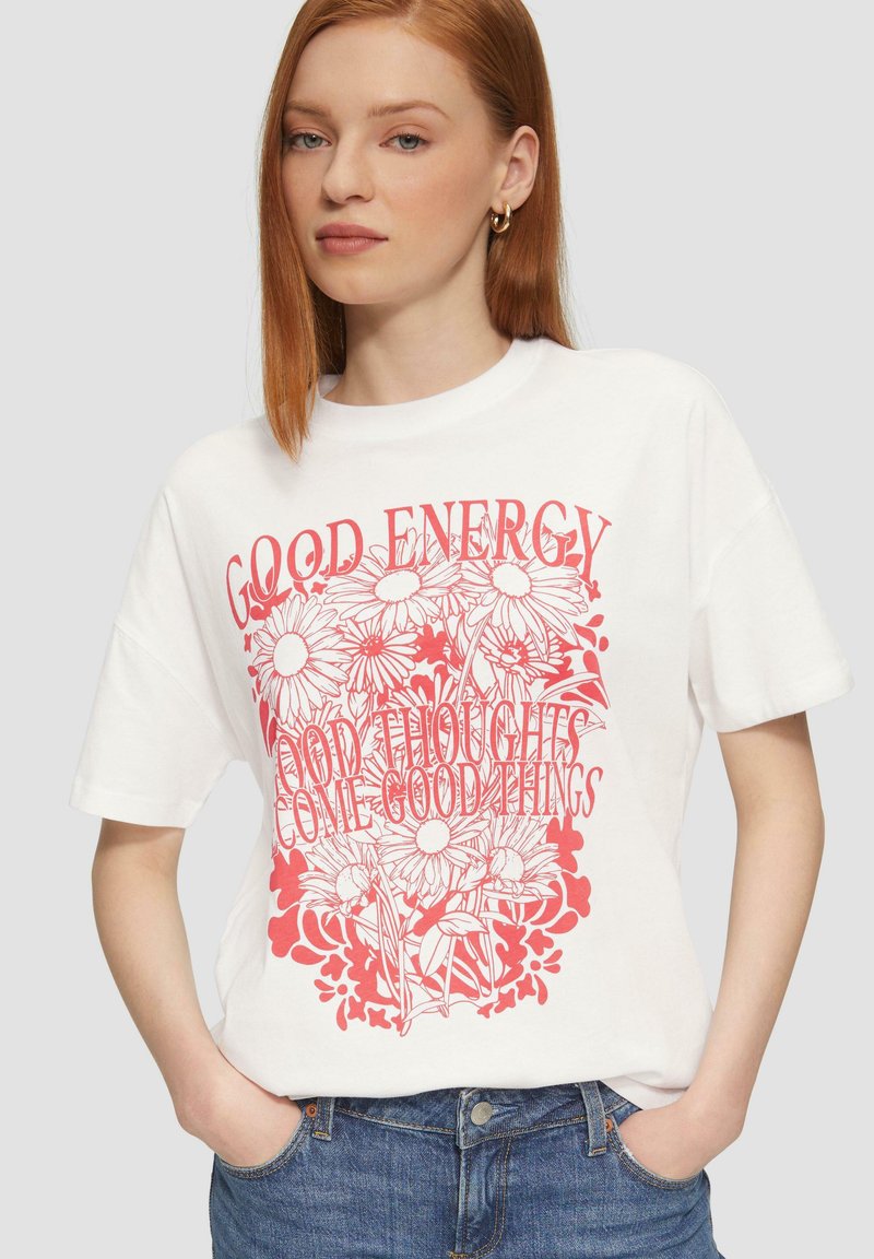 Witte katoenen t-shirt met een rode bloemenprint en de tekst "GOEDE ENERGIE" en "GOEDE GEDACHTEN KUNNEN GOEDE DINGEN BRENGEN." Relaxte pasvorm, korte mouwen.