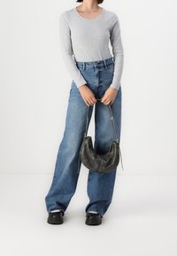 Grå långärmad ribbad skjorta i kombination med höga blå vida jeans. Modellen håller en liten svart läder hobo-väska med silverdetaljer.