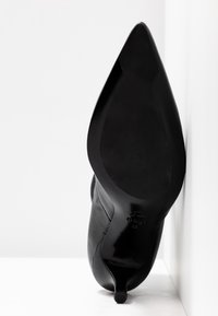 Černá kožená vysoká bota na podpatku se špičatou špičkou a hladkým povrchem. Obsahuje štíhlý stiletto podpatek a elegantní podrážku.