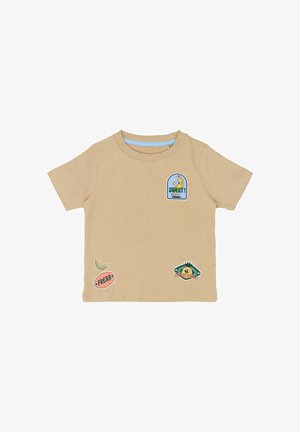 Beige bomulds-T-shirt med korte ærmer, prydet med flerfarvede mærker: en banan, en blå label med teksten "SWEET!" og forskellige grafiske elementer.