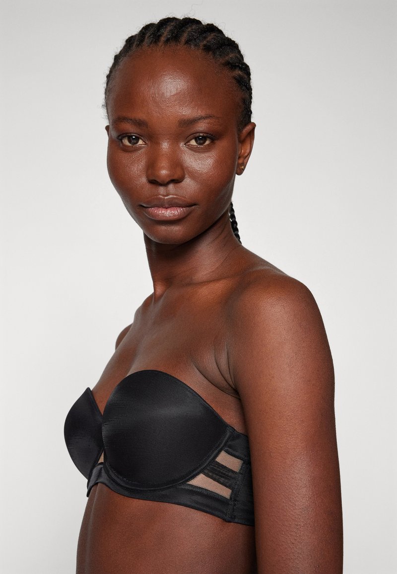 Soutien-gorge noir sans bretelles avec un tissu lisse, soutien-gorge à armatures et accents en panneau translucide sur les côtés, conçu pour un maintien sûr.