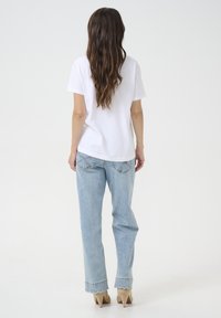 T-shirt en coton blanc, léger, à manches courtes. Jeans en denim bleu clair avec ourlet en vagues et coutures décoratives. Chaussures à talons beiges.
