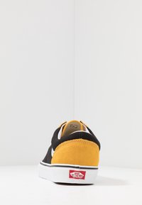 Black and yellow canvas sneaker with a suede heel, white stripe, and black sole. Features 'Vans Off The Wall' logo on the heel.
