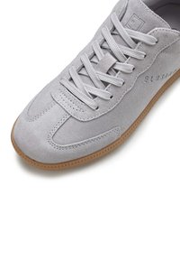 Hellgraue Wildleder-Sneaker mit flachen Schnürsenkeln, Gummisohle und subtilen Logodetails. Runde Zehenpartie und sauberes Design mit strukturierten Akzenten.