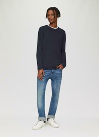 Marineblauwe trui met lange mouwen en witte kraag, gecombineerd met lichtblauwe rechte spijkerbroek en witte sneakers met zwarte accenten.