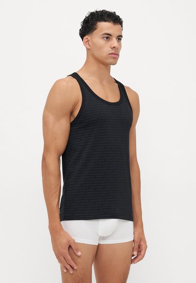 Schwarzes Tanktop mit einem tonalen Logomuster, aus glattem Stoff gefertigt. Verfügt über breite Träger und einen lässigen Schnitt, getragen über weißen Unterhosen.