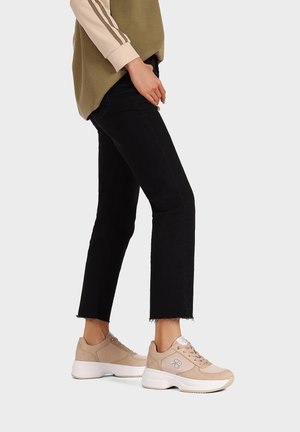 Sneaker beige con una parte superiore in suede e mesh lisci, caratterizzati da una suola bianca spessa e dettagli con logo. Abbinati a jeans neri a vita bassa.
