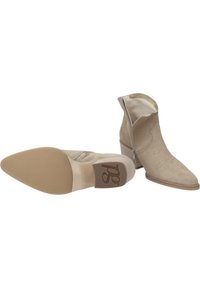 Botines de ante color beige con puntera afilada, costuras decorativas y una cremallera lateral. Cuentan con un tacón bajo y apilado y una suela lisa.